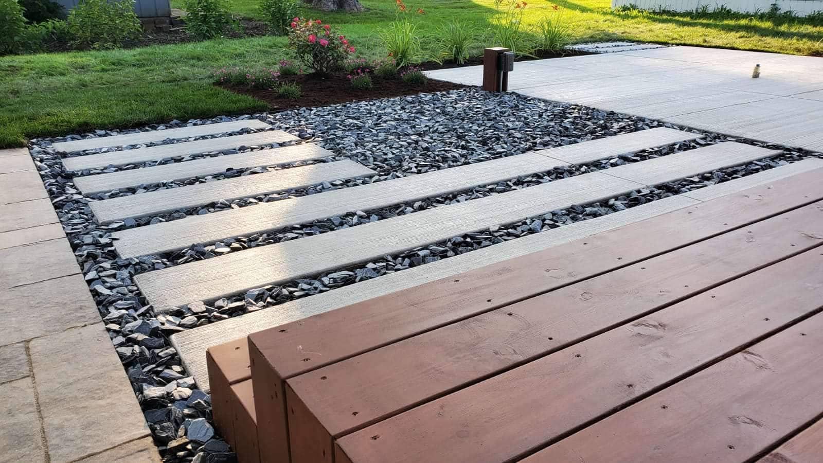 A wooden deck transitions to stepping stones and dark rocks, leading to grass.