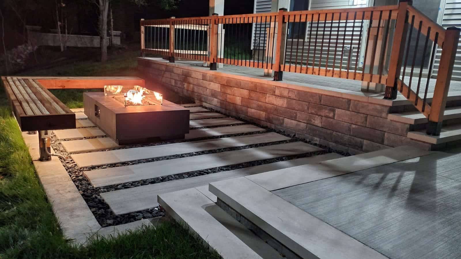 Modern backyard patio with stone steps, brick fire pit, and railing at night