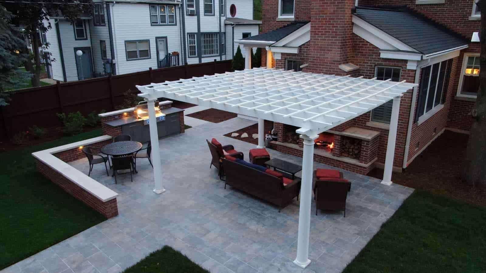 Backyard patio with white pergola, outdoor seating, and string lights beside a house