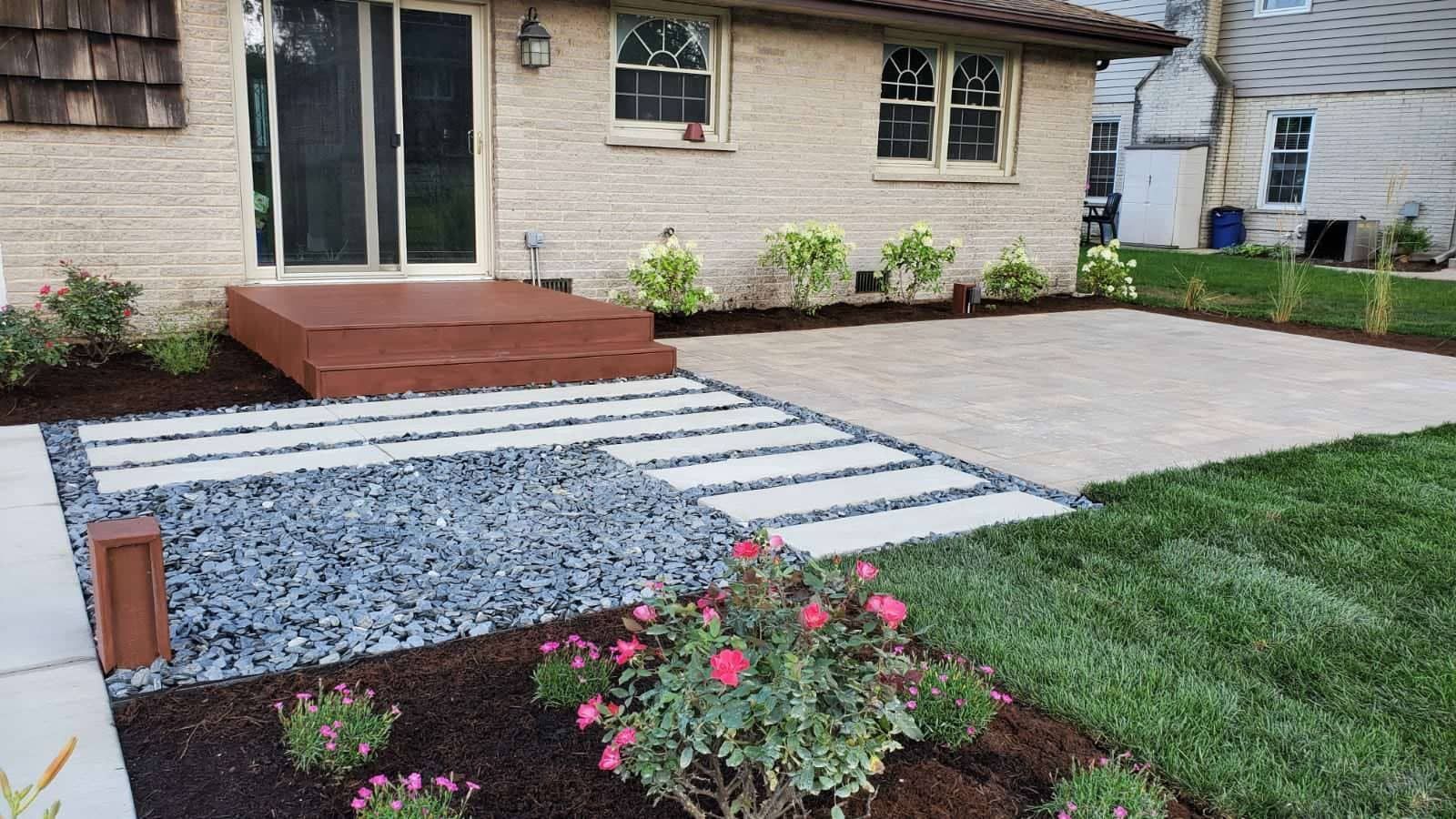Front yard landscape with stone walkway, gray gravel, pink flowers, and a house porch.