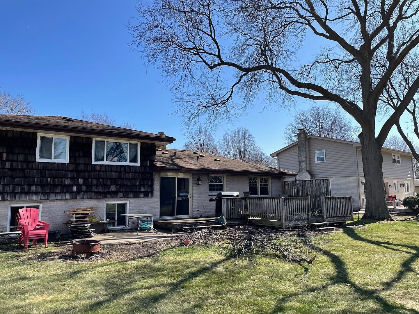 Backyard with two-story house, deck, and large bare tree in front of a blue sky.