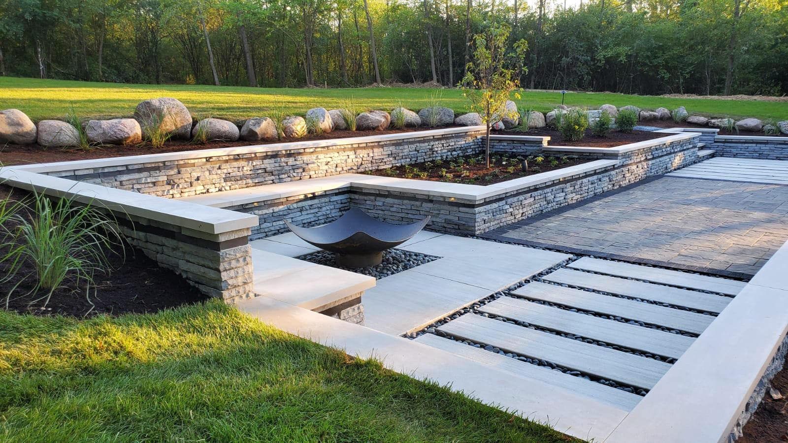 Modern backyard with stone retaining walls, pathways, and a fire pit.