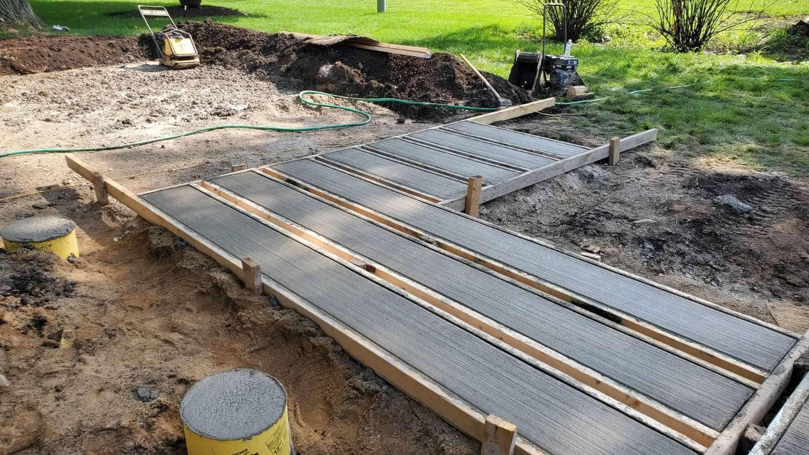 Wooden forms for a concrete walkway under construction in a yard, with dirt and equipment visible.