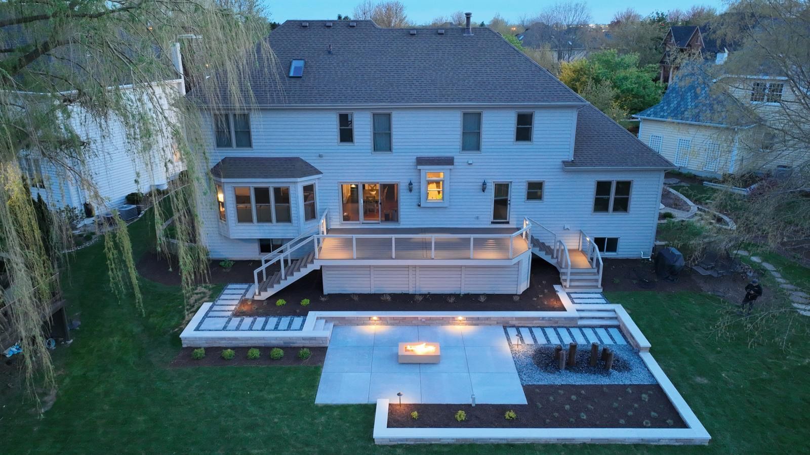 White two-story house with a lit backyard deck and patio at dusk, viewed from above