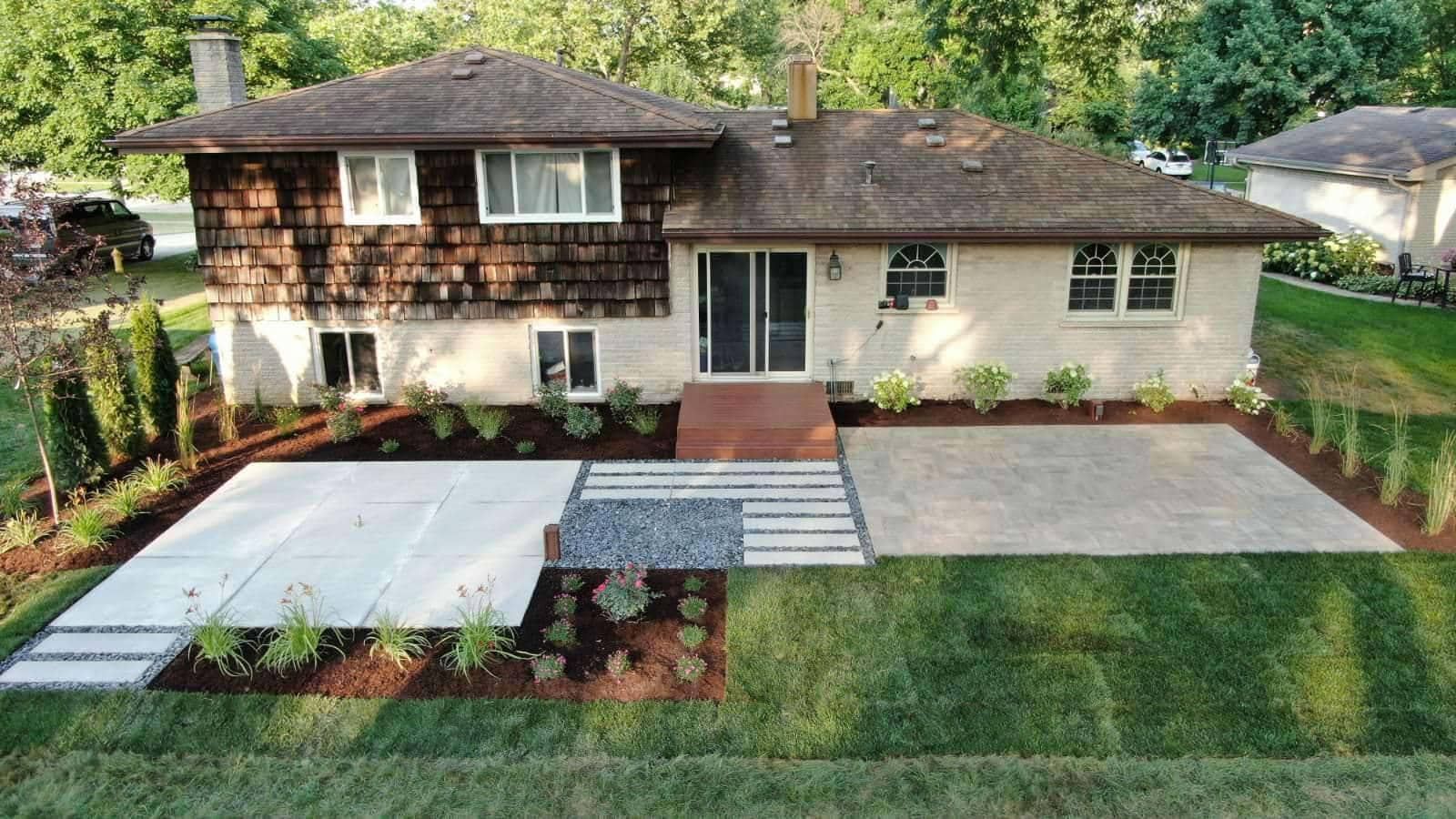 Two-story house with a new patio, walkway, and landscaping, surrounded by green grass.
