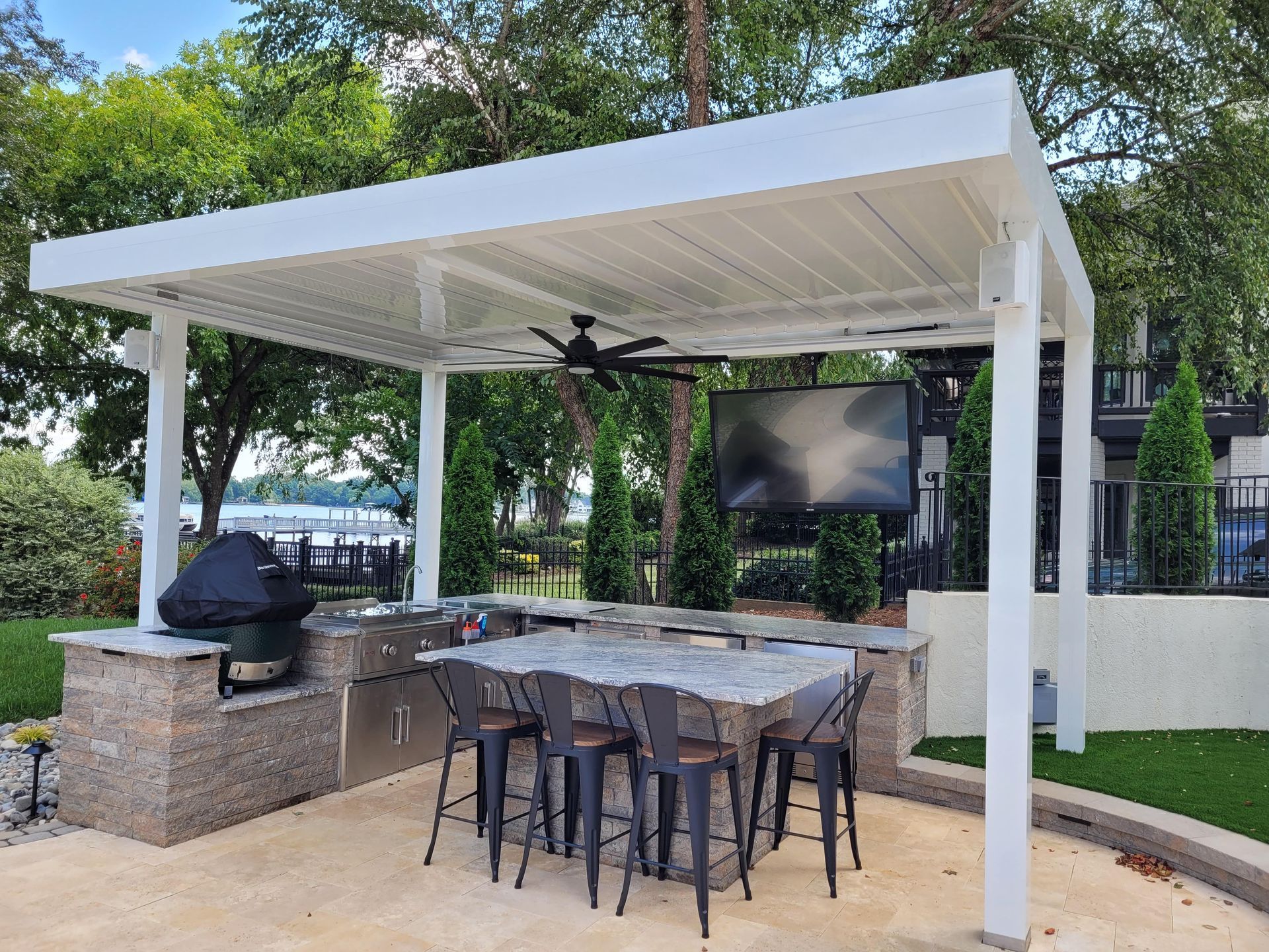 Covered outdoor patio with dining table, grill, and TV beneath a white pergola