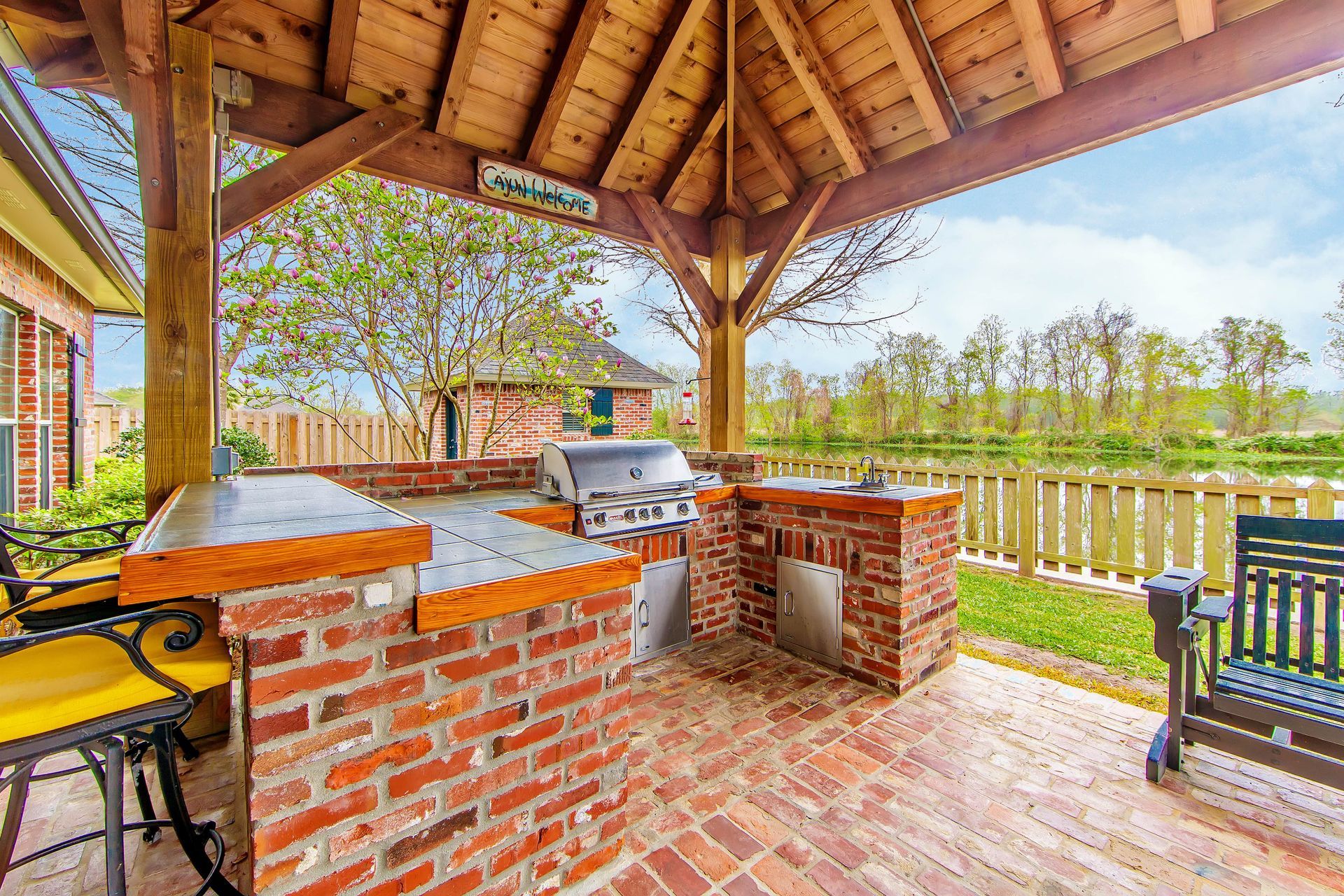 Outdoor brick kitchen with grill, seating, and gazebo overlooking a body of water.
