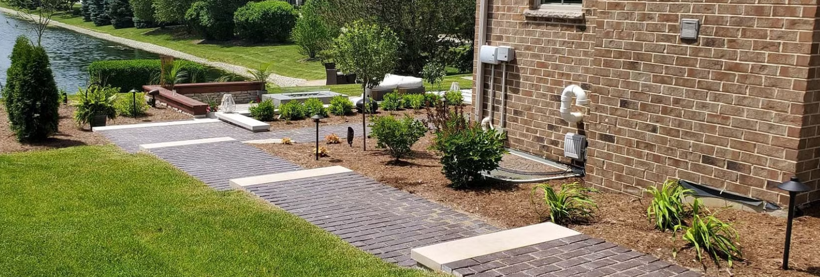 Landscaped yard with brick pathway leading to a building and garden with a water view.