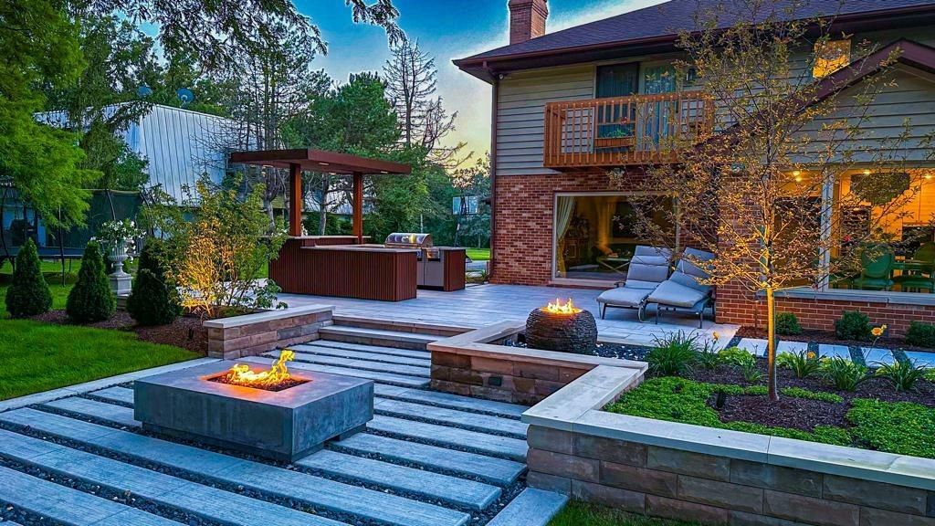Backyard patio with a fire pit, wooden deck, stone steps, and a house beside lush green landscaping