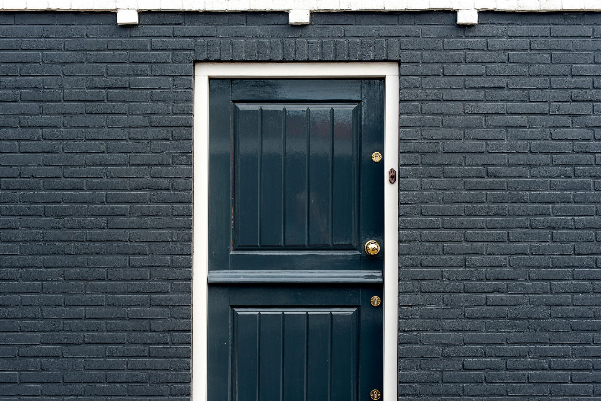 Dark blue door with brass knobs set in a dark brick wall with white trim