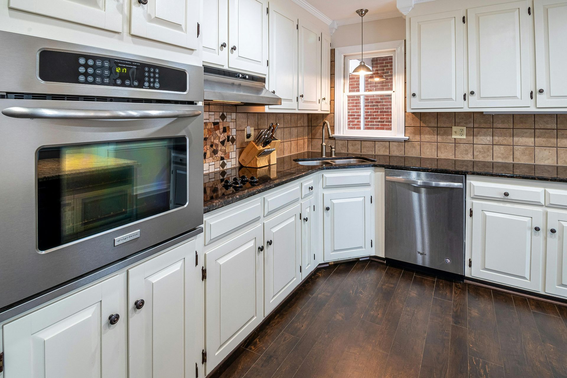 Bright kitchen with white cabinets, stainless steel appliances, dark wood floor, and beige tile backsplash.