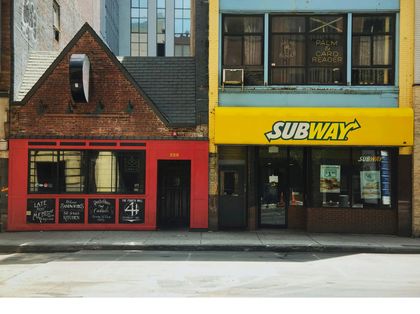 Streetfront of a red brick restaurant next to a yellow Subway sandwich shop