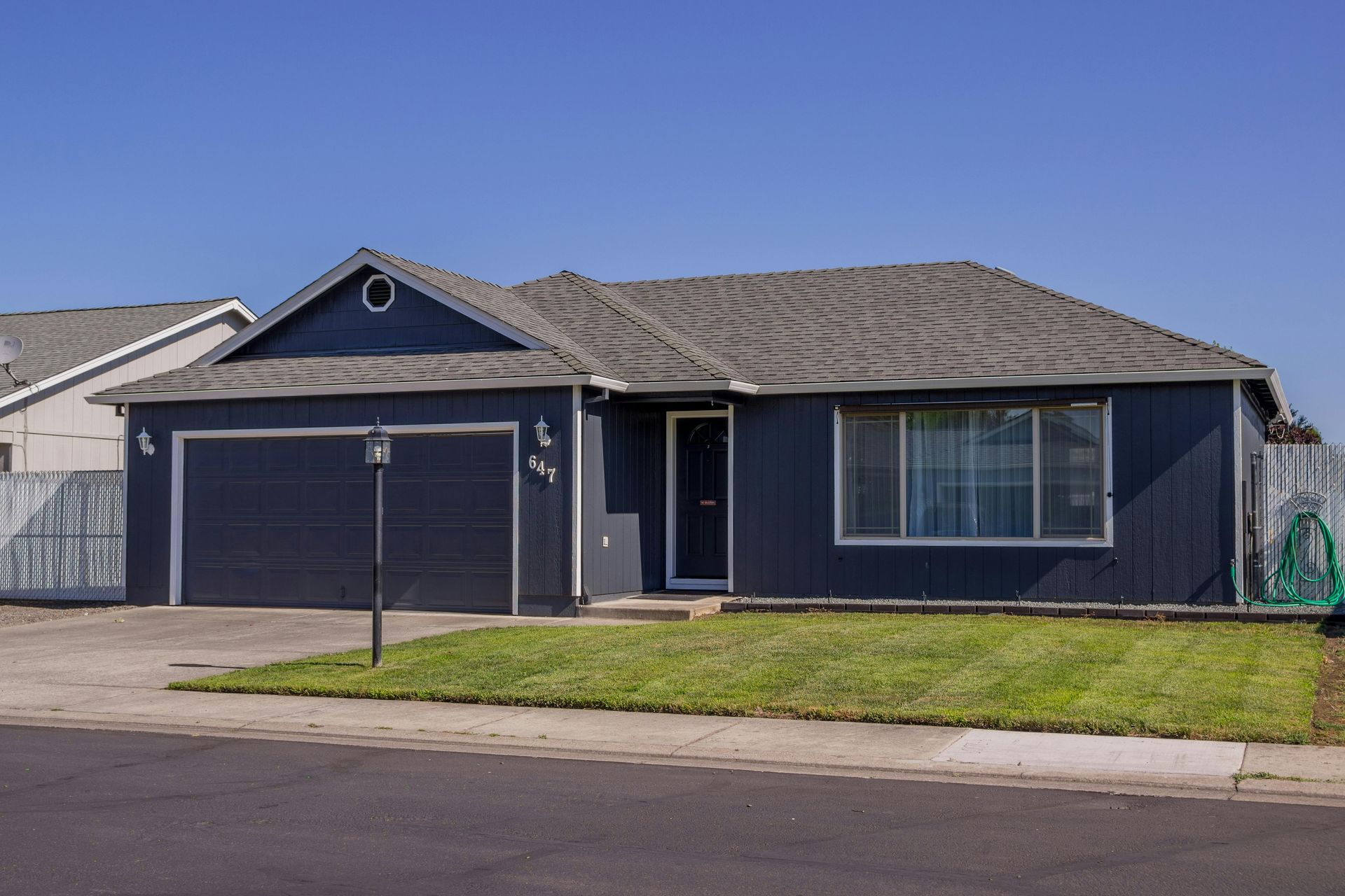 Single-story blue house with a two-car garage and small front lawn on a quiet street