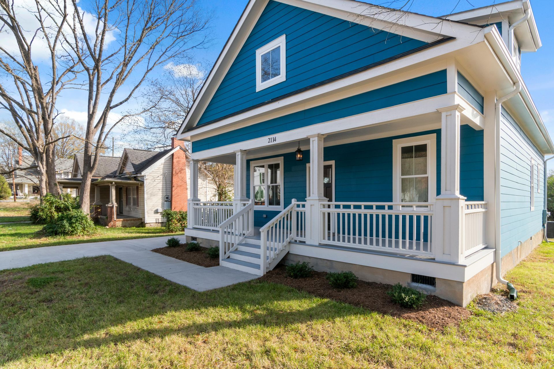 Blue-and-white house with a front porch and steps, set beside a sidewalk on a sunny day