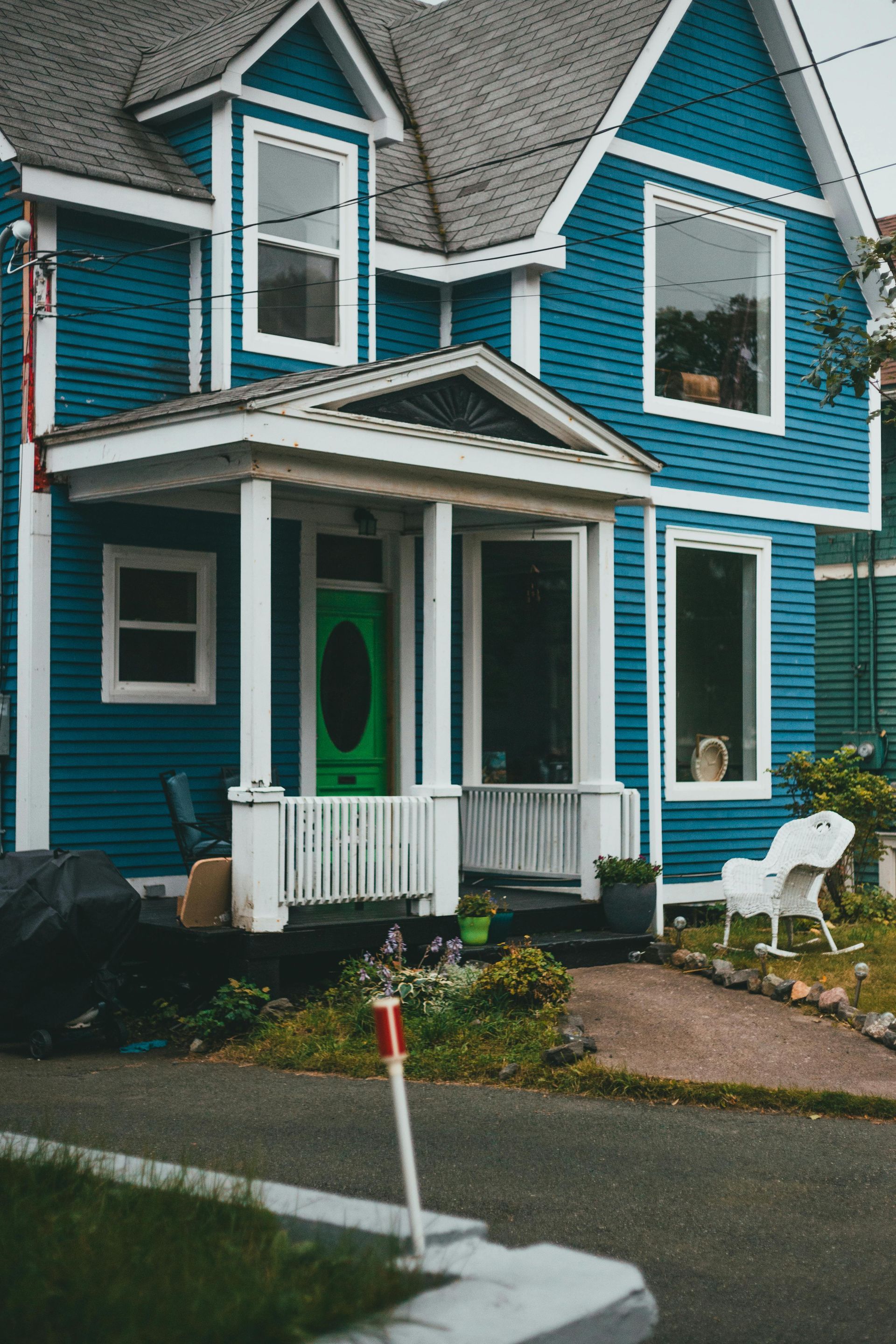 Turquoise two-story house with white trim and a small front porch beside a wet street.