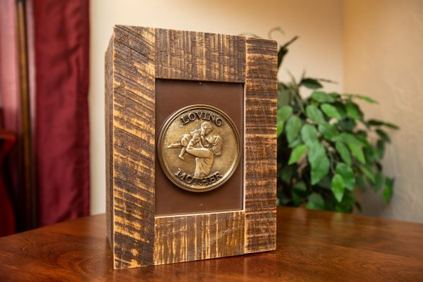 Wooden box with a bronze medallion. The medallion depicts people embracing; it’s set against a brown background.