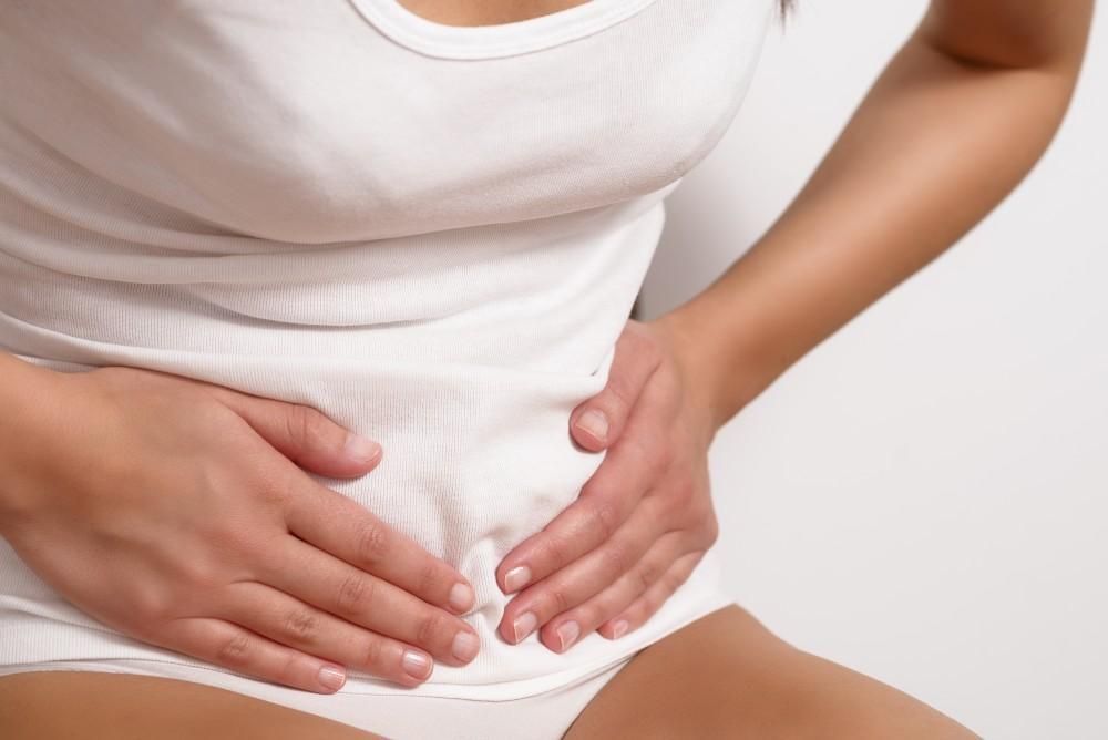 Woman in white clothing holding her abdomen, likely experiencing abdominal pain.