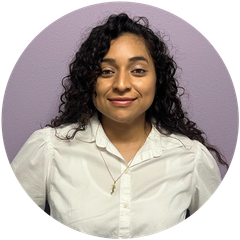 Woman with curly hair wearing a white collared shirt, smiling, against a purple background.