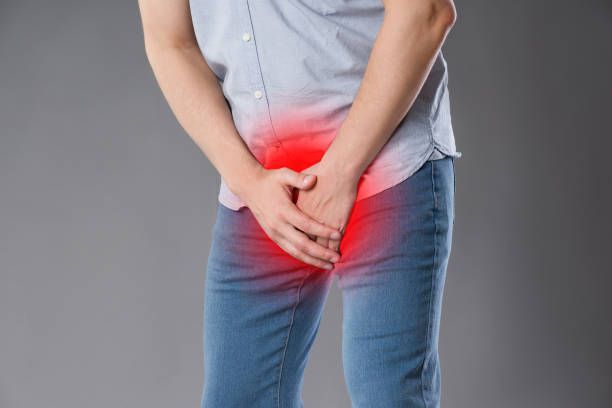 Man in casual clothing holding pelvic area, highlighting post-prostatectomy discomfort.