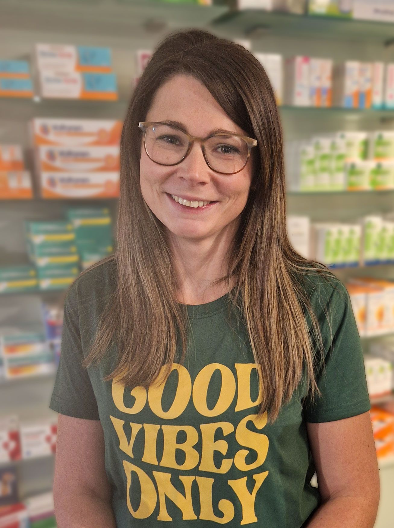 Eine Frau mit Brille und einem grünen T-Shirt mit der Aufschrift „Good Vibes Only“ steht in einer Apotheke.
