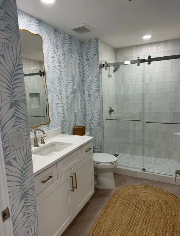 Bright modern bathroom with white vanity, toilet, glass shower, and woven rug