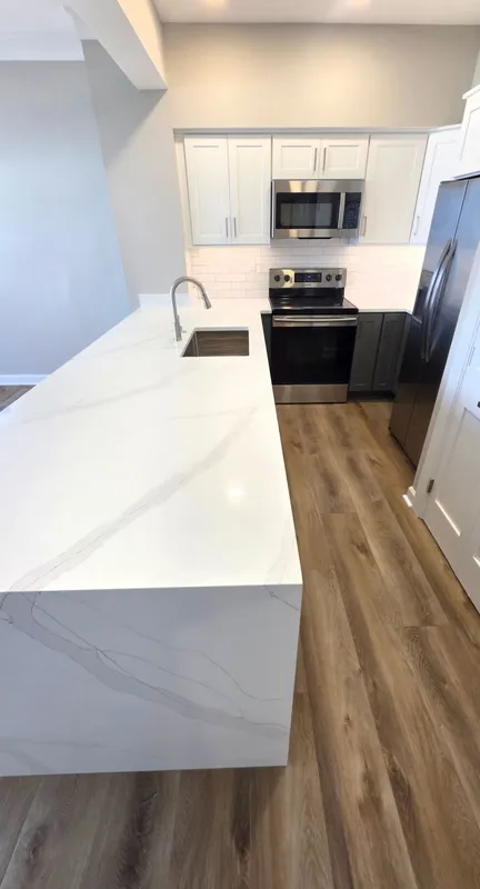 Modern white kitchen with island, stainless steel appliances, and wood-look flooring