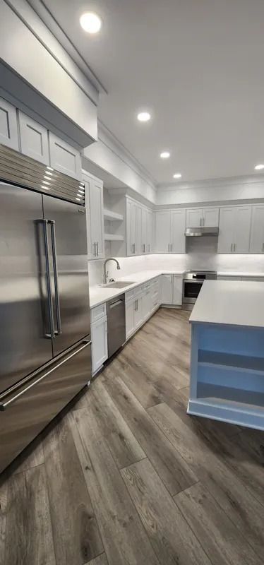 Bright modern kitchen with stainless steel appliances, white cabinets, and gray wood flooring