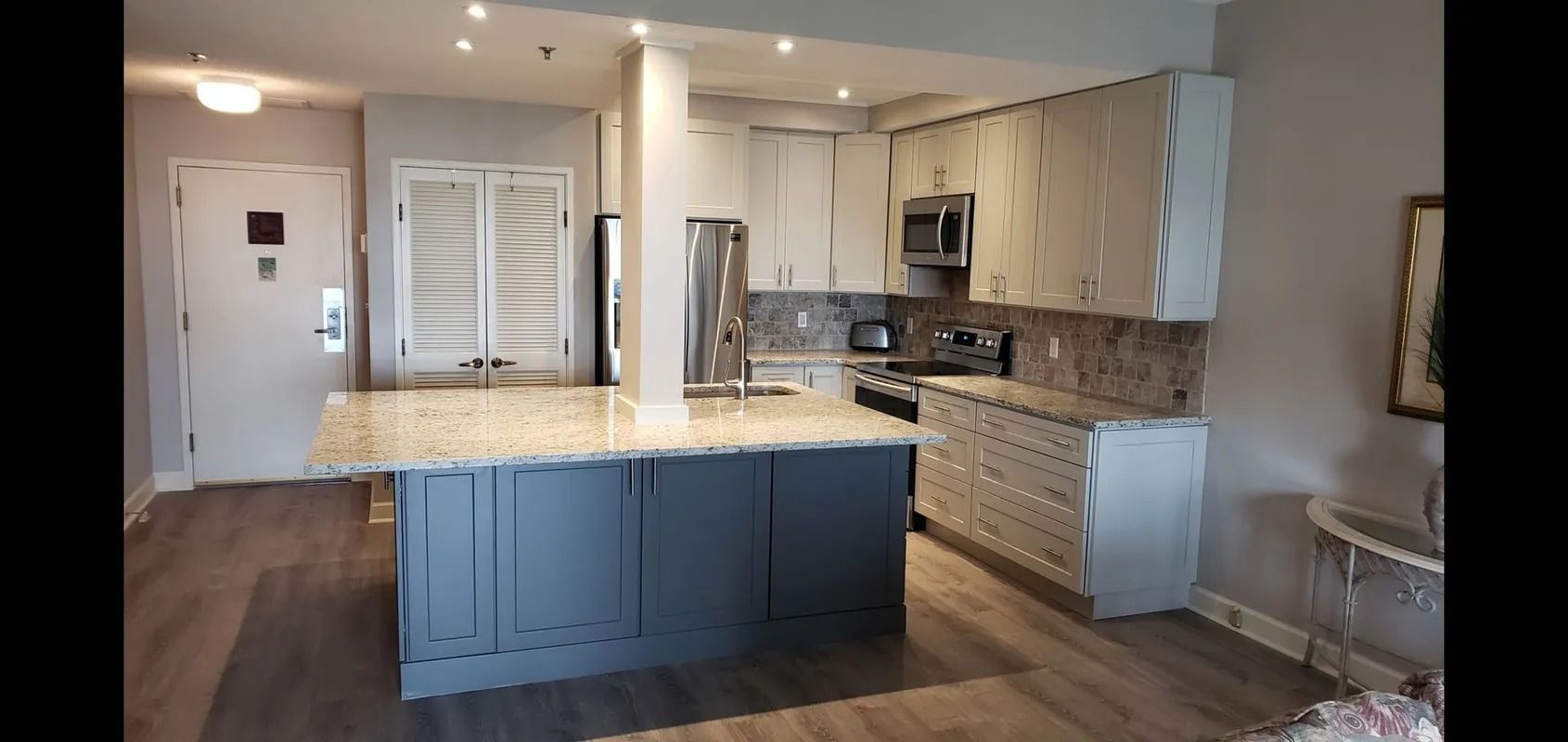 Modern kitchen with white cabinets, gray island, stainless appliances, and wood floors