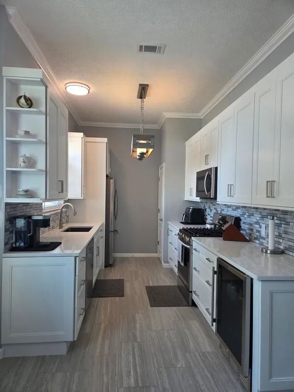 Bright galley kitchen with white cabinets, stainless appliances, and light wood flooring