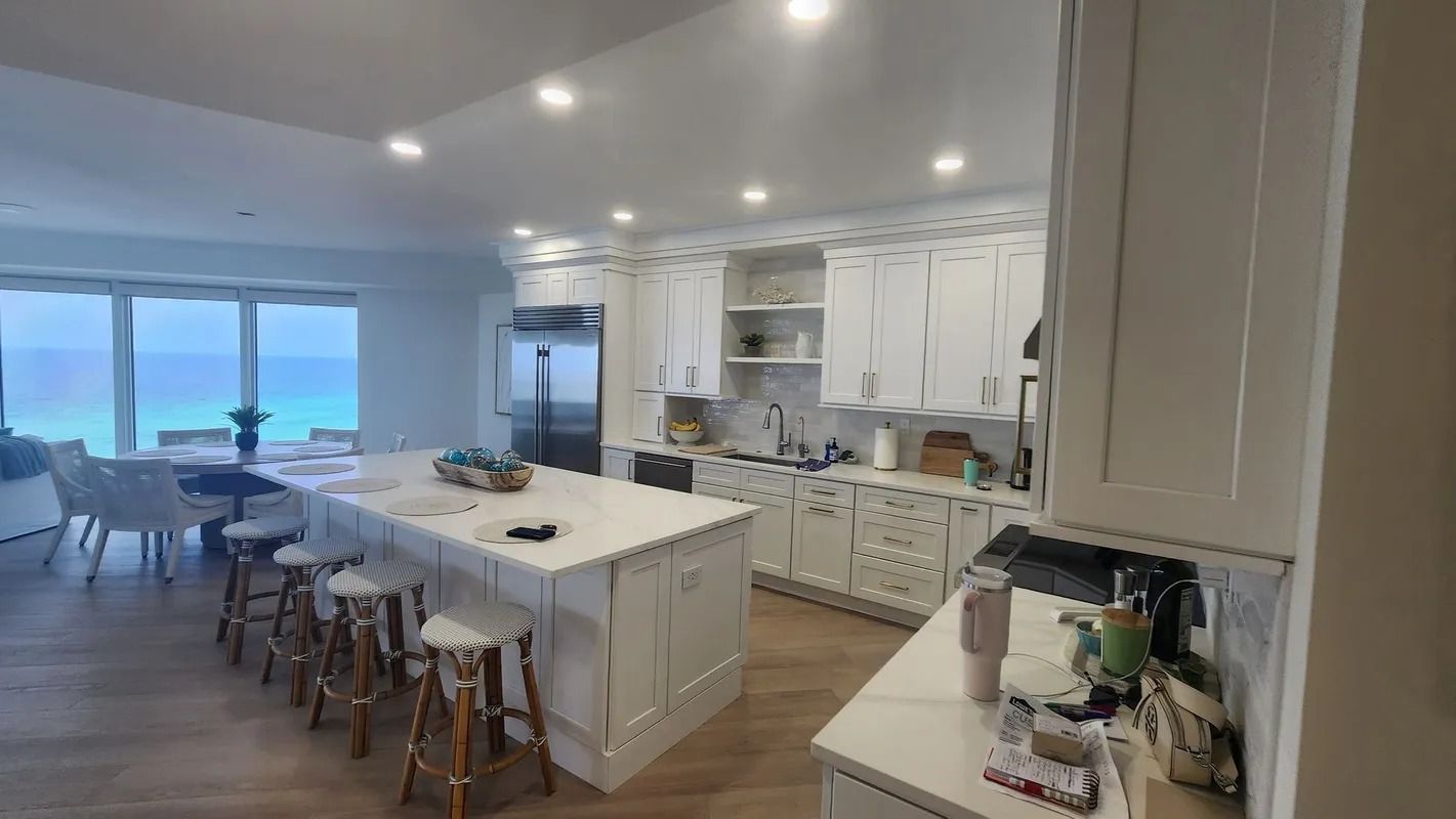Bright open kitchen and dining area with white cabinets, island seating, and ocean-view windows
