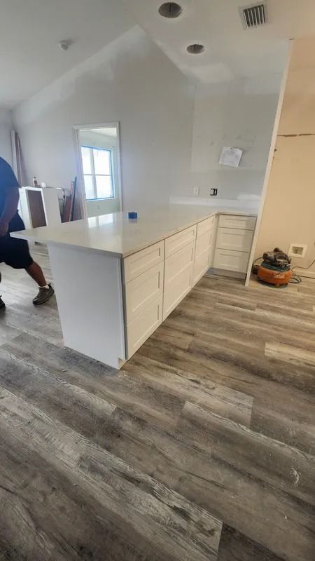 Kitchen renovation with white island cabinets, gray wood-look floor, and a partially painted wall