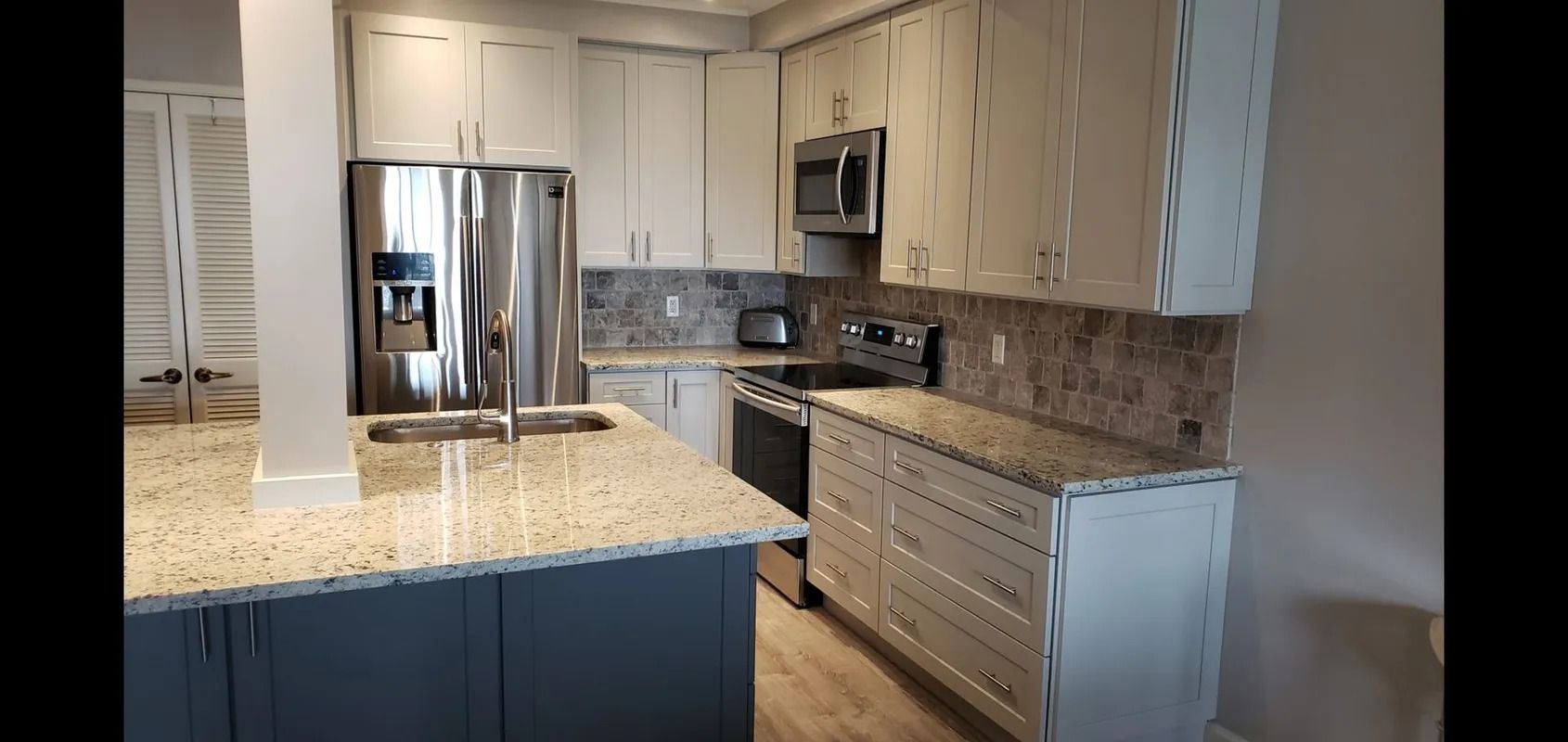 Bright modern kitchen with stainless steel fridge, light cabinets, and granite countertop peninsula