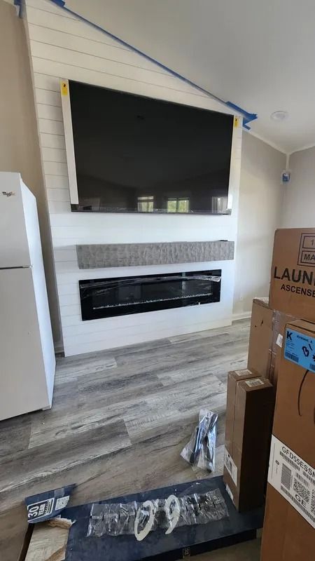 Living room with a large black wall-mounted TV above a long fireplace and boxes on the floor