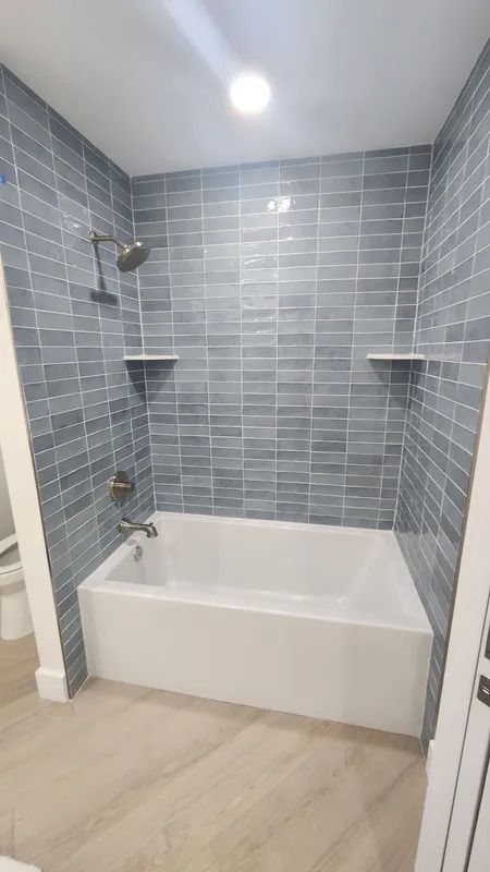 Walk-in bathtub with gray tile walls, white tub, and beige wood-look floor in a bathroom