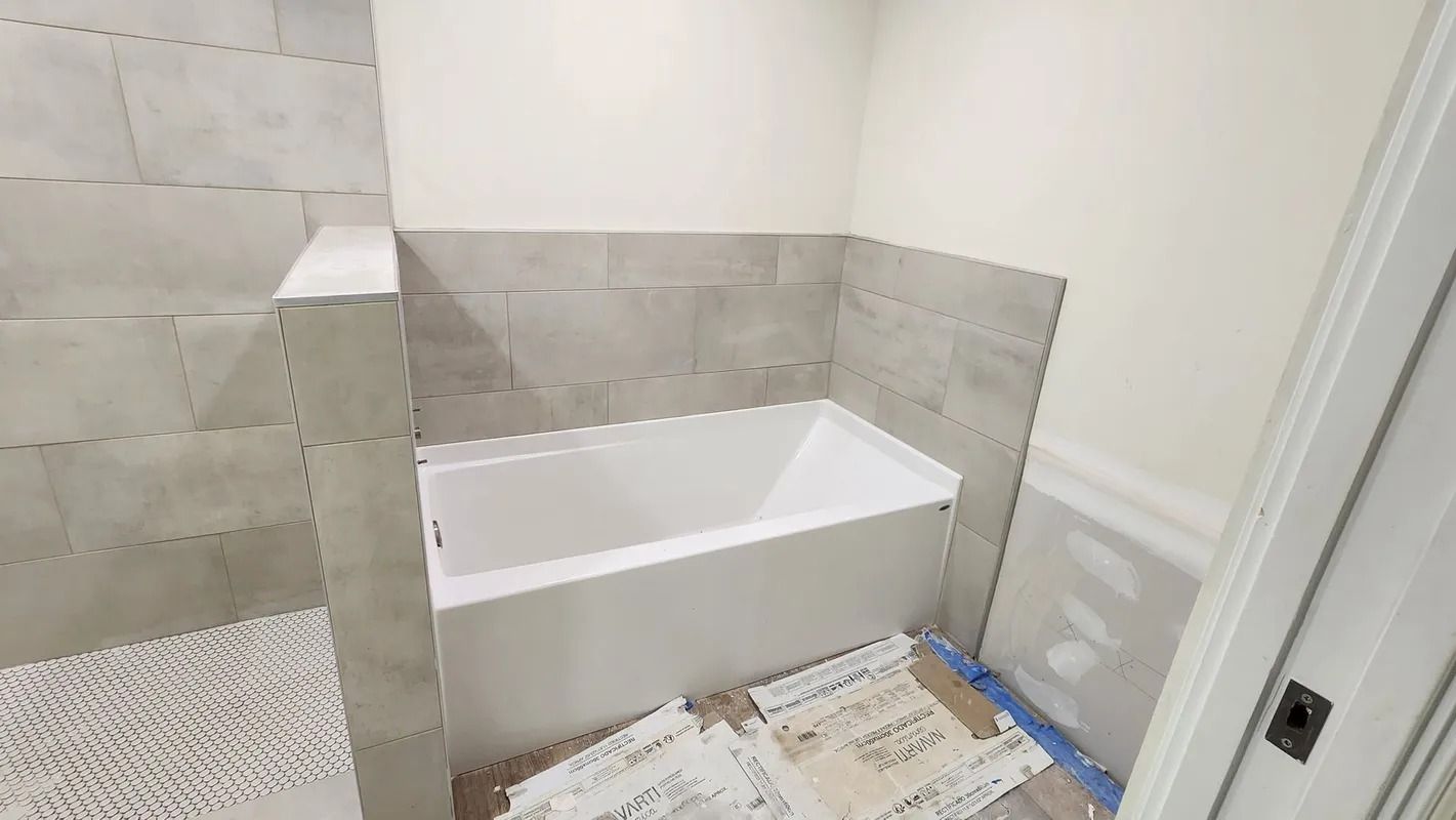 Partially tiled bathroom with a white bathtub under renovation, floor covered with protective paper.