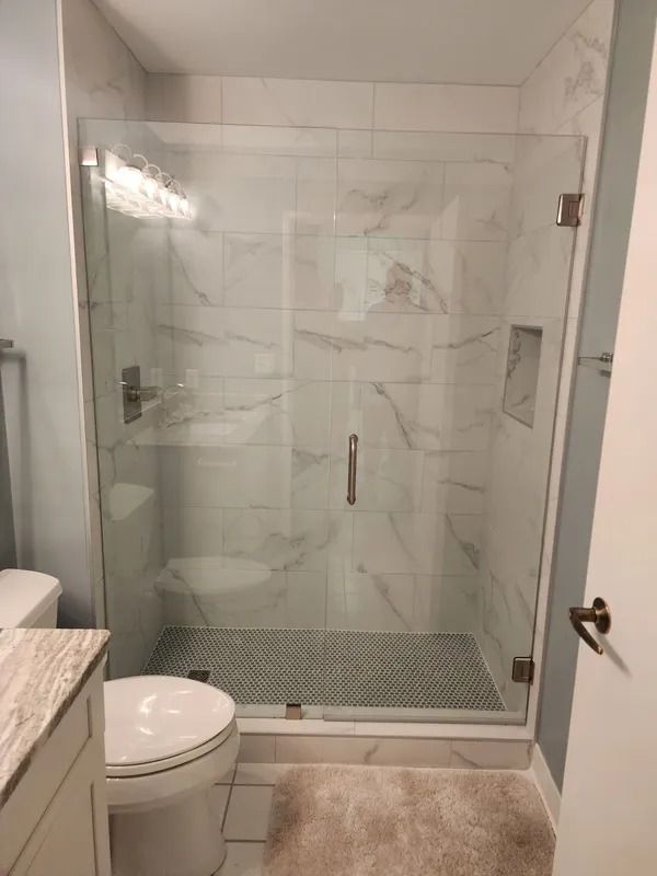 Modern bathroom with glass walk-in shower, toilet, and marble-pattern tile.