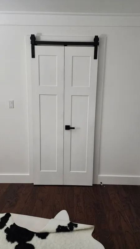 White double closet doors with black barn-style track on a white wall, over dark wood floor.