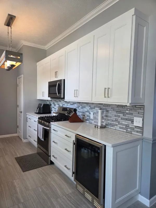 Modern white kitchen with gray tile backsplash, stainless appliances, and wood-look floor