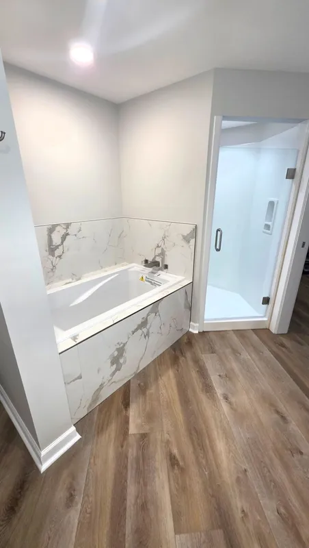 Modern bathroom with white vanity, marble walls, wood-look floor, and glass shower door.