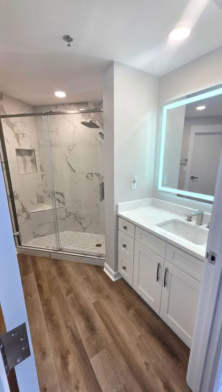Modern bathroom with wood-look floor, double vanity, and tiled shower with glass door