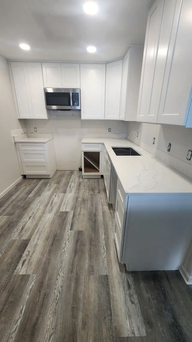 Bright white galley kitchen with gray wood-look floors, white cabinets, and a central island.