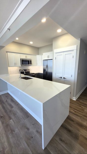 Bright modern kitchen with white cabinets, peninsula, recessed lights, and wood-look flooring