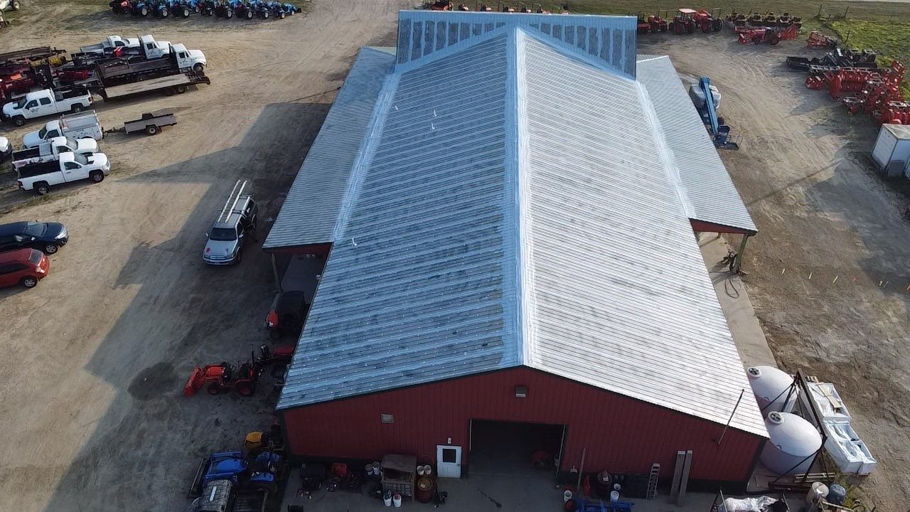 Red barn with silver roof; vehicles and equipment parked around it.