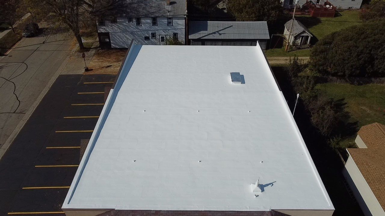 Aerial view of a white flat roof on a building, surrounded by parking lot and other buildings.