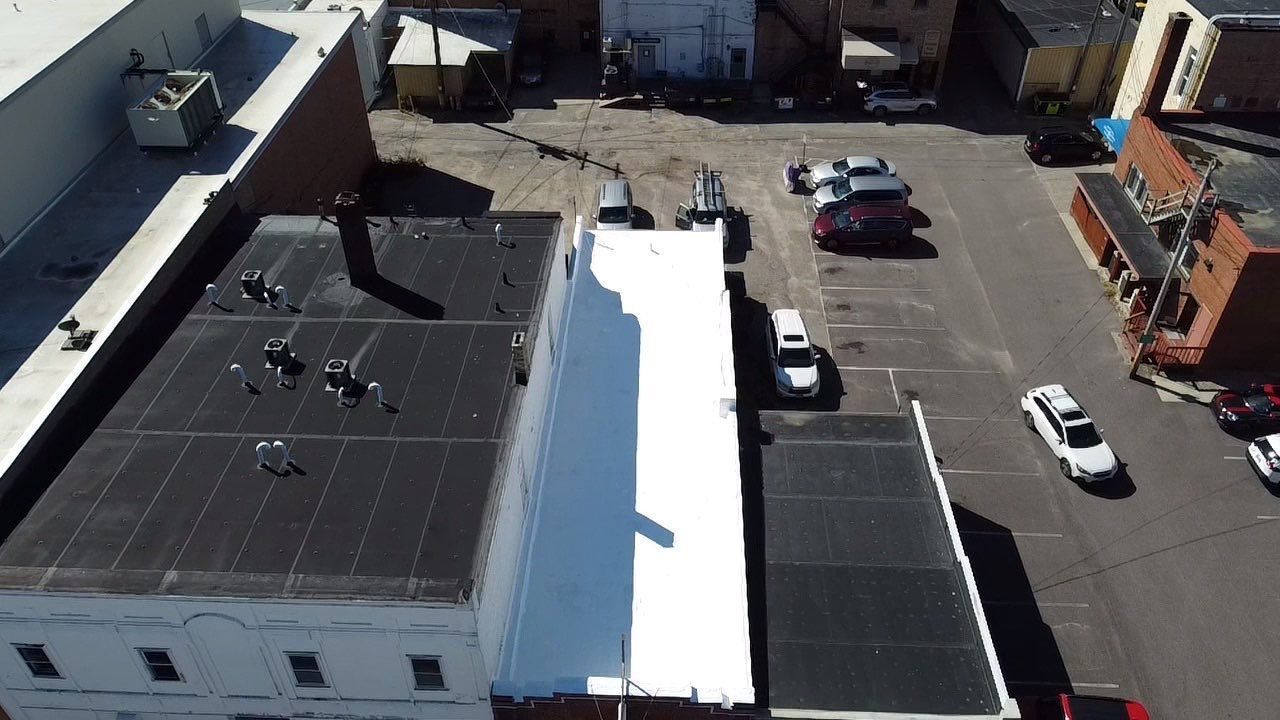 Aerial view of city buildings with cars parked in a lot and on the street. Black and white roofs.
