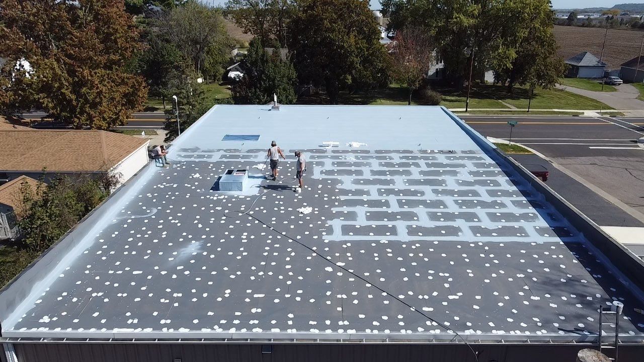 Workers installing roofing on a large, flat, gray roof of a commercial building.