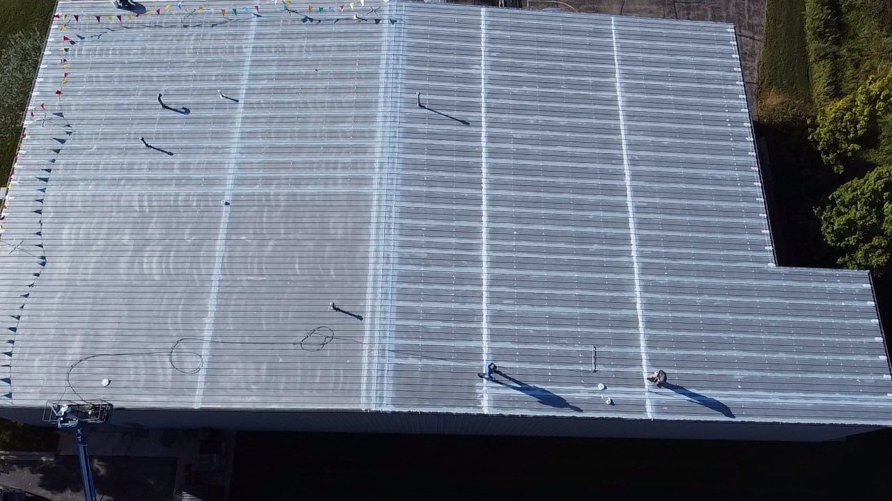 Overhead view of a flat rooftop covered with netting. Shadow of person and trees visible around the edges.
