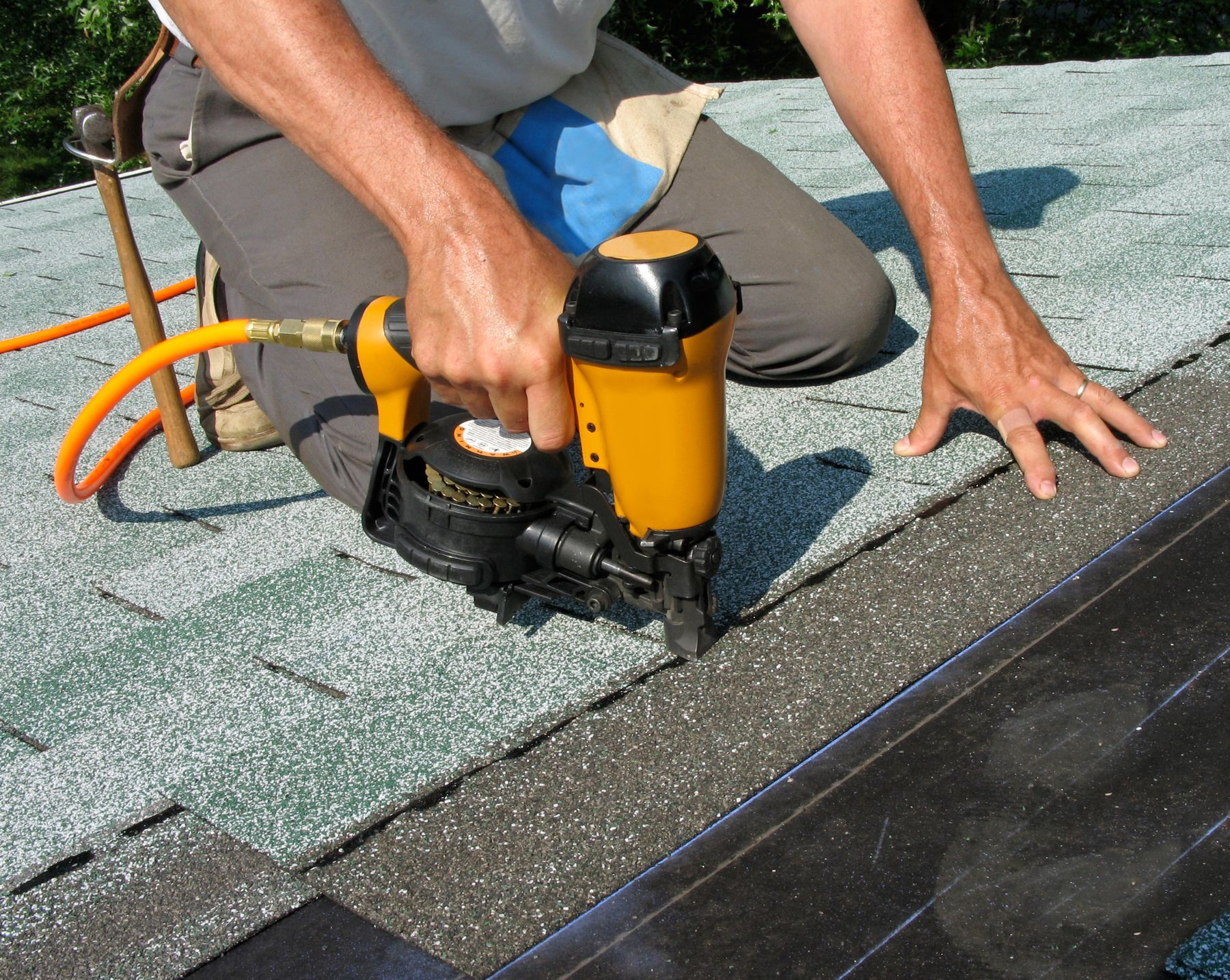 Close-up of a roofer from a roofing company, performing roof repair with a yellow nail gun.