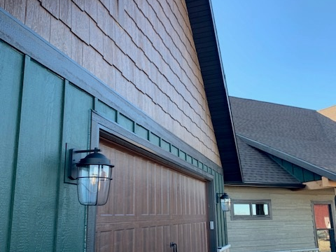 Exterior of a house featuring green siding, brown garage door, and cedar shake siding above.