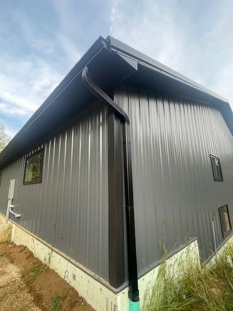 A large gray metal building with a black gutter on the side of it.